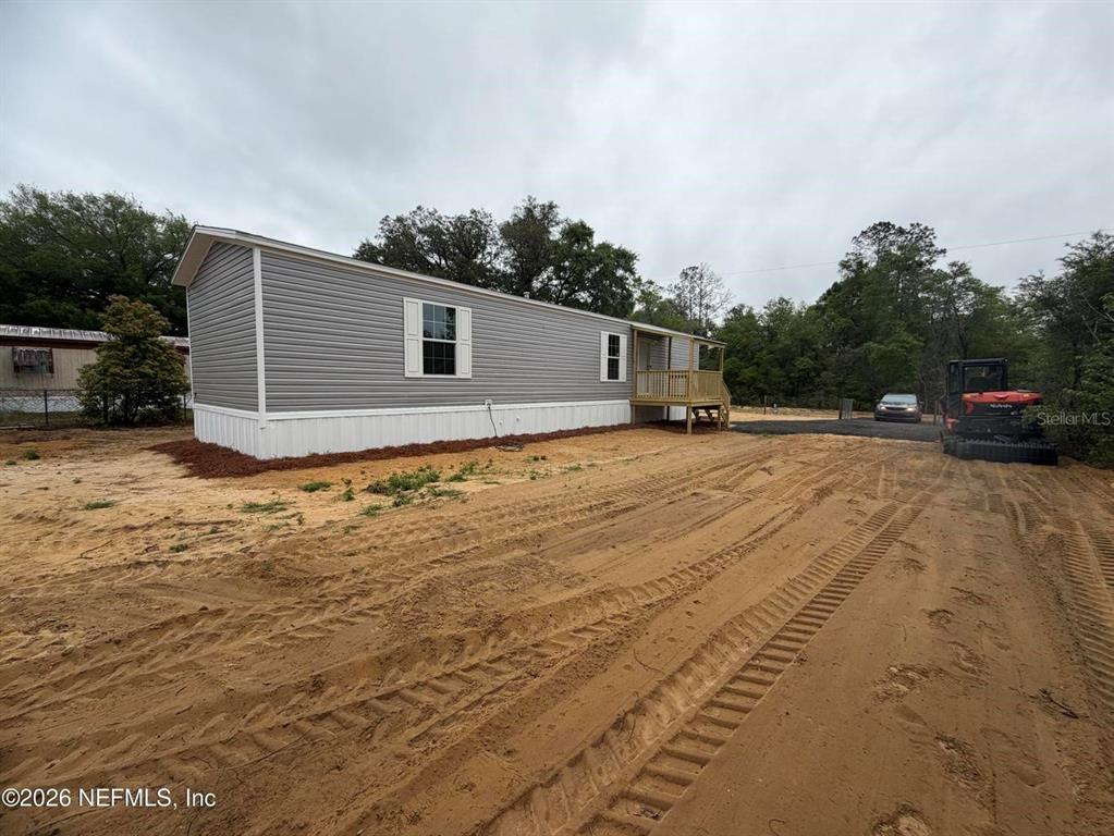 A single-story manufactured home with gray siding sits on a dirt lot with a deck — 213 MILTON AVENUE, INTERLACHEN, FL