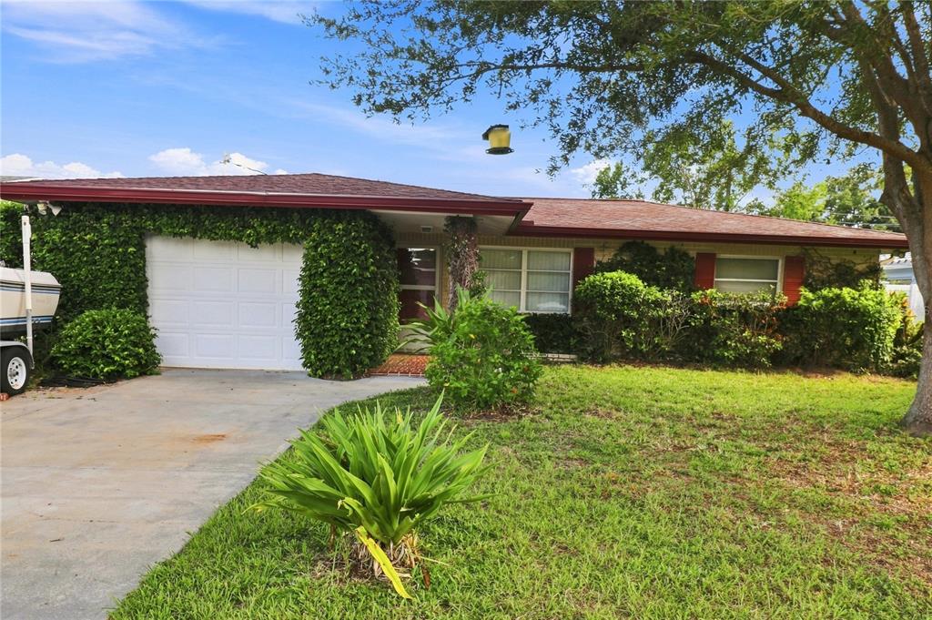 A single-story house with a white garage door, overgrown greenery, and a concrete driveway — 1070 6TH AVENUE NE, LARGO, FL