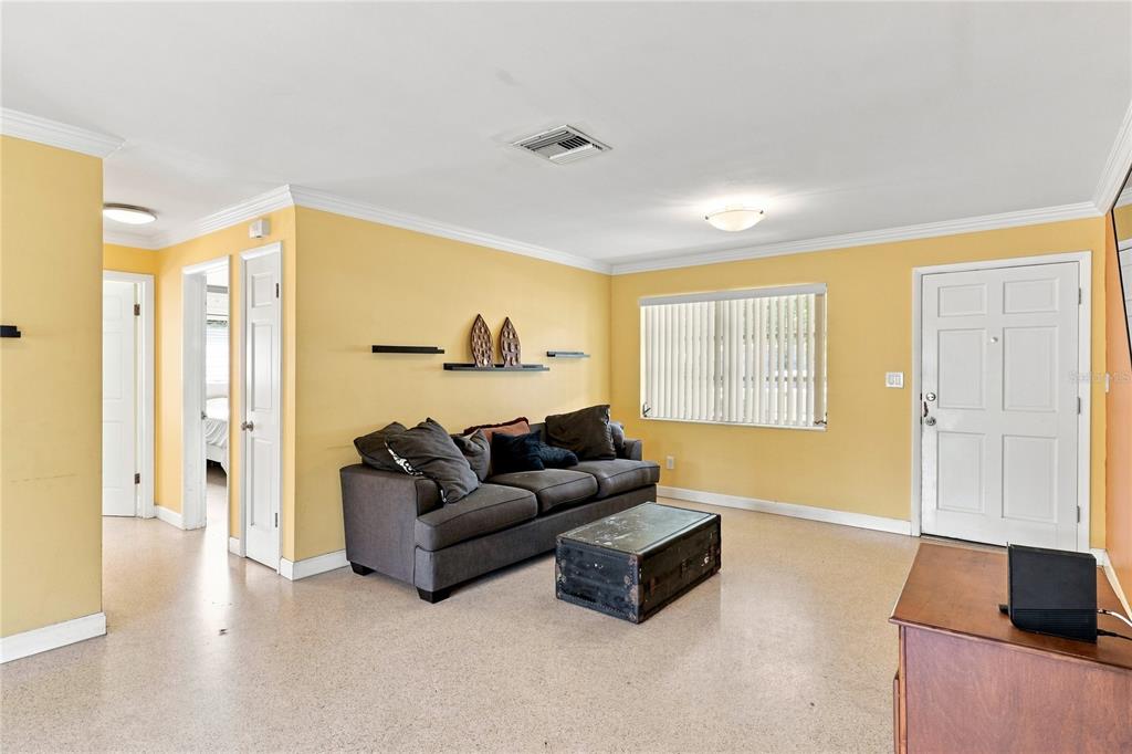 A living room with yellow walls, a gray sofa, a trunk coffee table, and tile flooring — 1070 6TH AVENUE NE, LARGO, FL