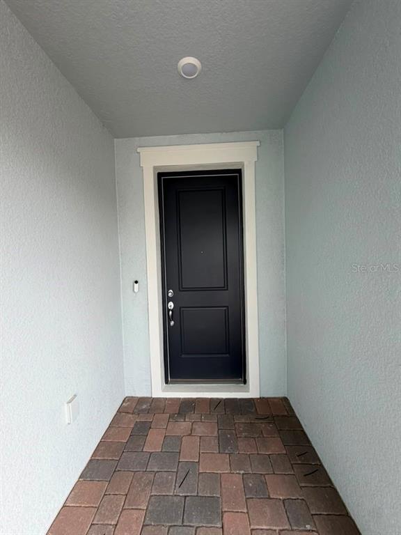 A black front door with white trim is set within a covered entryway with paver flooring — 467 WINTER GROVE BOULEVARD, WINTER GARDEN, FL
