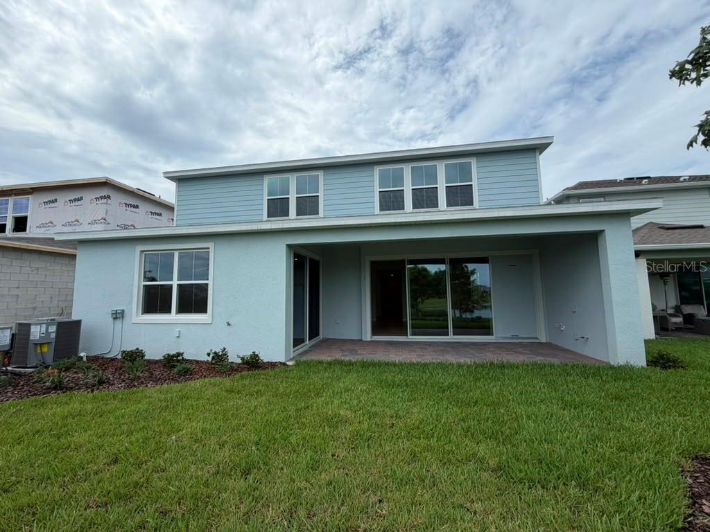 The rear exterior of a two-story light blue house features a covered patio and lawn — 467 WINTER GROVE BOULEVARD, WINTER GARDEN, FL