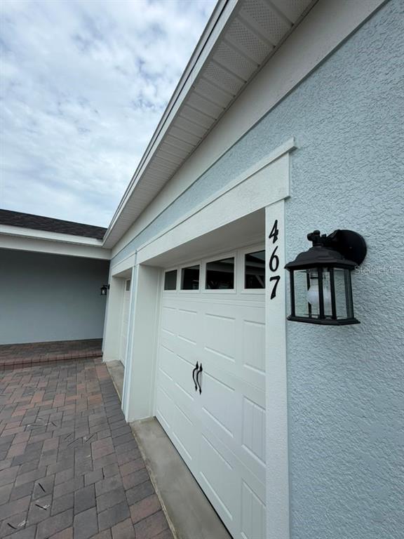 A light blue exterior wall features a white garage door, a black lantern, and house numbers — 467 WINTER GROVE BOULEVARD, WINTER GARDEN, FL