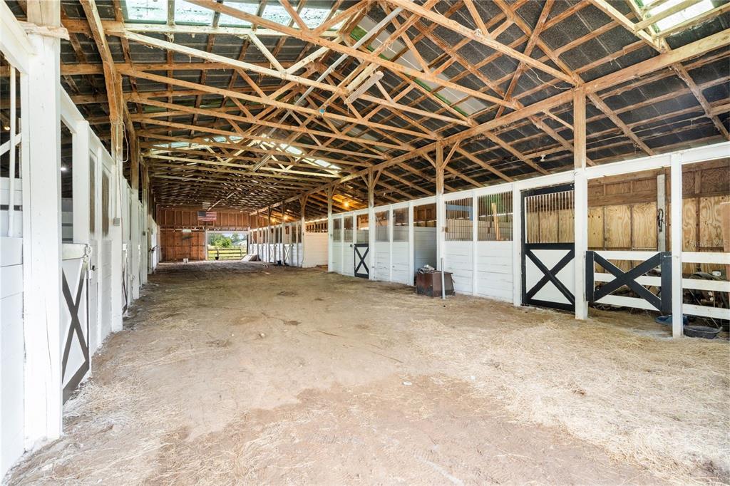An interior view of a rustic horse barn with multiple stalls and a dirt floor — 1750 SW 17TH TERRACE, BELL, FL
