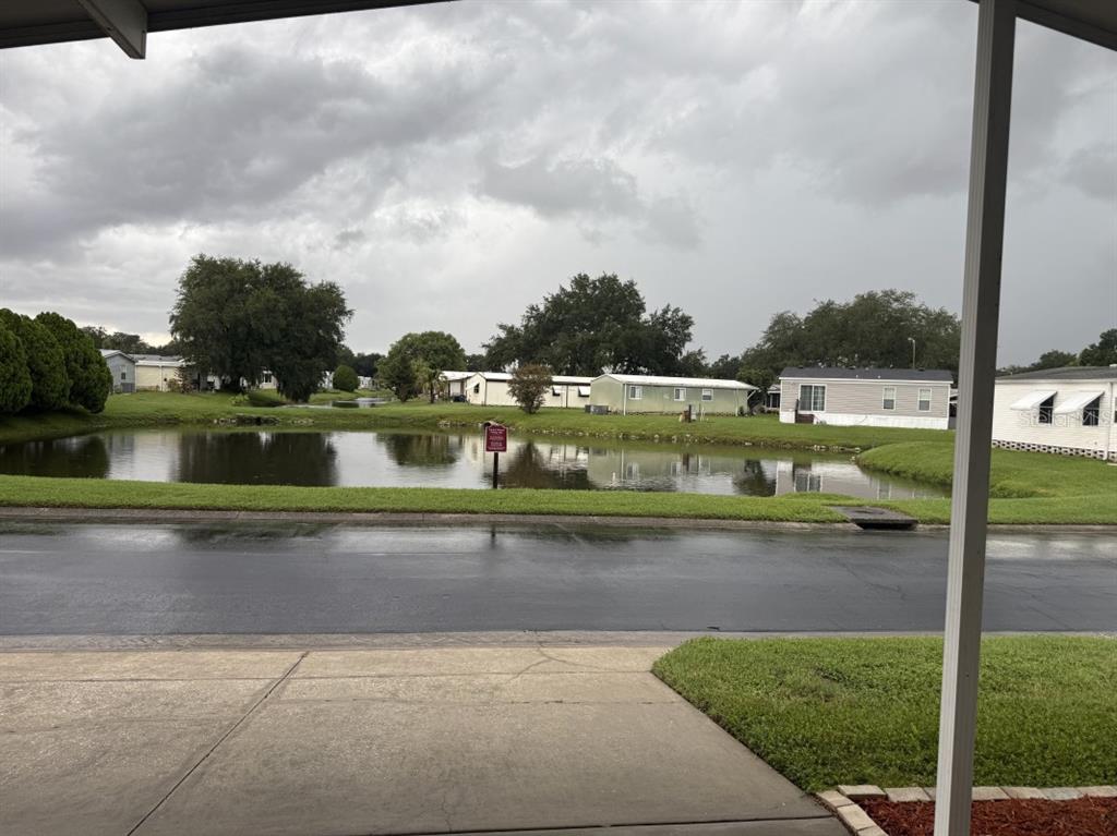 A view from a covered porch overlooking a pond and mobile homes under cloudy skies — 3104 SHADY CREEK DRIVE, WESLEY CHAPEL, FL