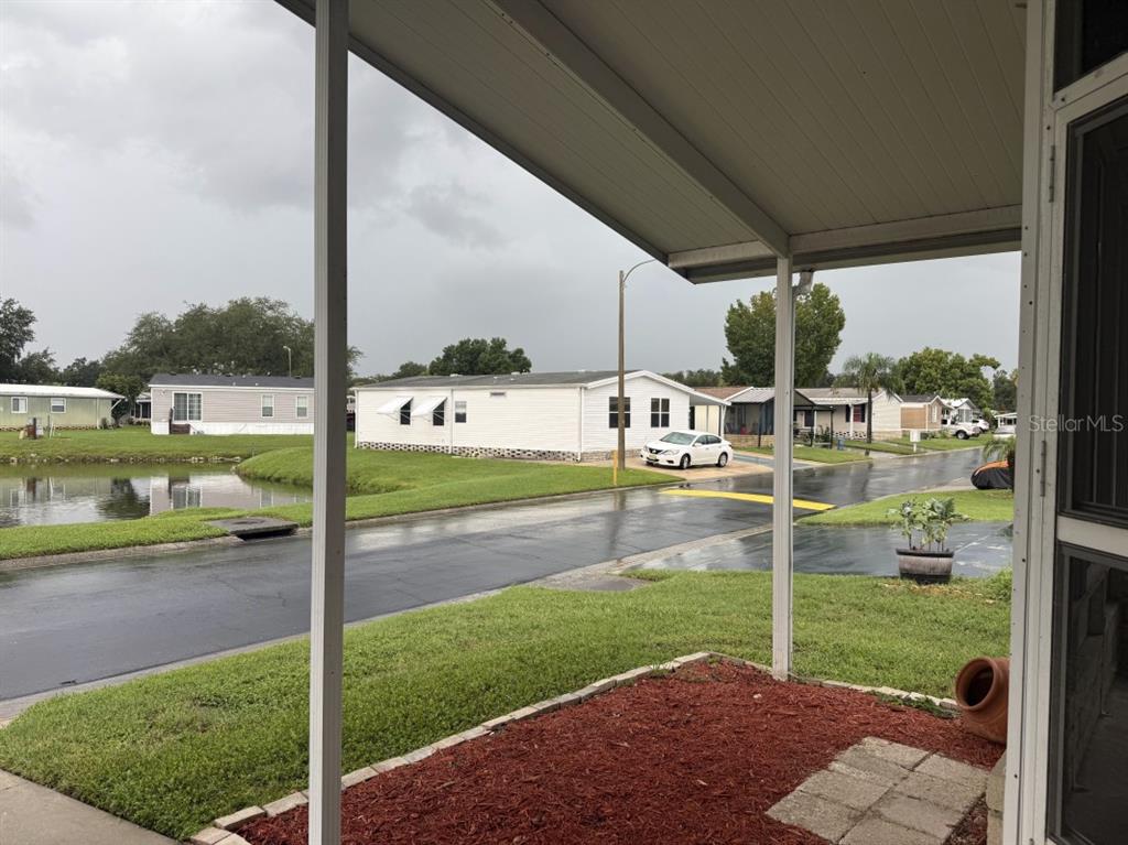 A view from a covered porch overlooking a residential street, a pond, and neighboring homes — 3104 SHADY CREEK DRIVE, WESLEY CHAPEL, FL