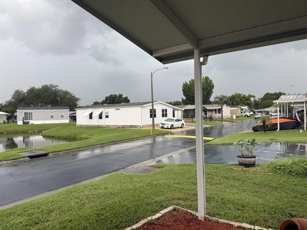 A view from a covered porch overlooking a wet street, mobile homes, and a pond — 3104 SHADY CREEK DRIVE, WESLEY CHAPEL, FL