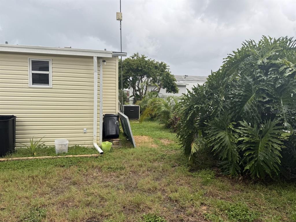 The exterior of a light-colored mobile home features a side window, downspout, and surrounding landscaping — 3104 SHADY CREEK DRIVE, WESLEY CHAPEL, FL