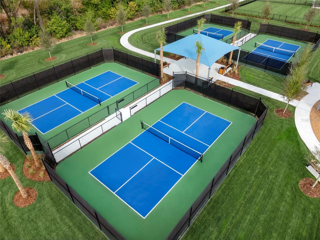 An aerial view shows multiple fenced pickleball courts with blue surfaces and a shaded seating area — 13007 SUNSEED STREET, PARRISH, FL