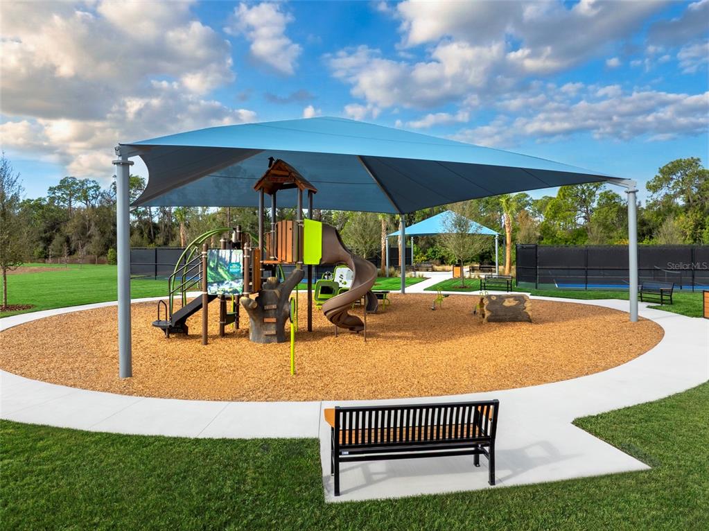 A playground with a large shade sail, play structure, and bench on a sunny day — 13007 SUNSEED STREET, PARRISH, FL