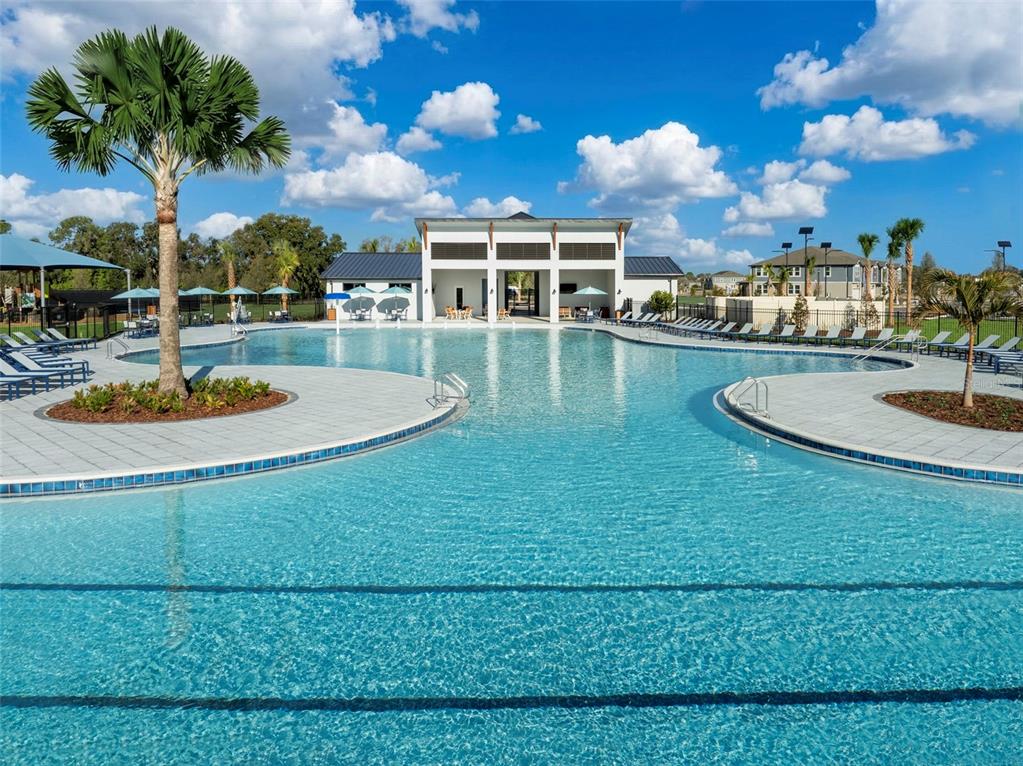 A large outdoor swimming pool with a central clubhouse and palm trees under a blue sky — 13007 SUNSEED STREET, PARRISH, FL