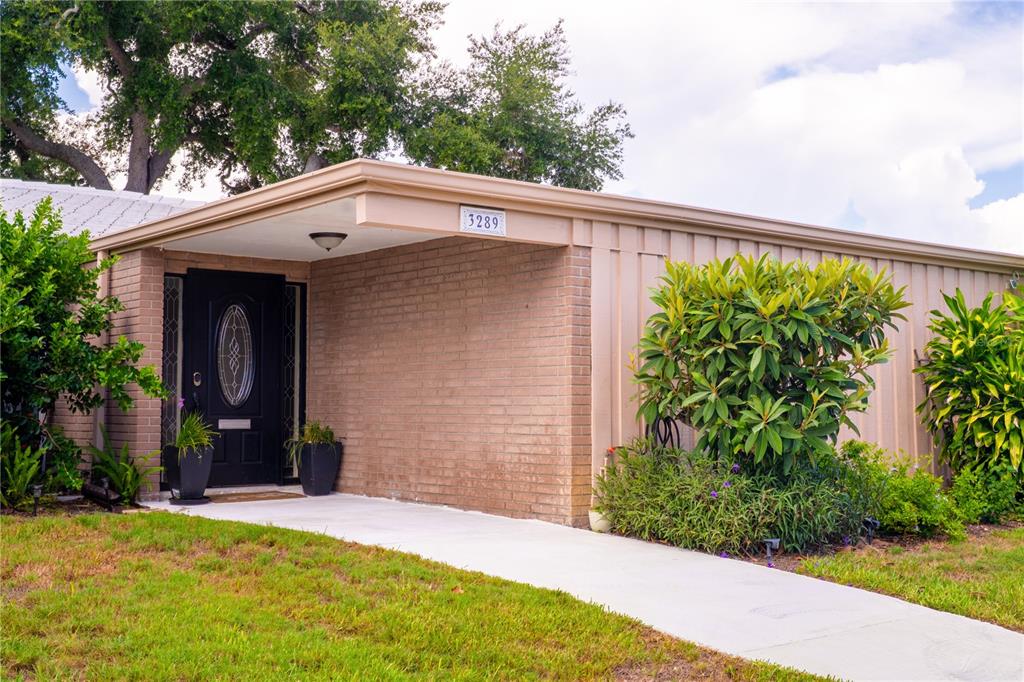 A single-story house exterior features a brick facade, a black front door, and a concrete walkway — 3289 FAIRHAVEN LANE UNIT 112, SARASOTA, FL