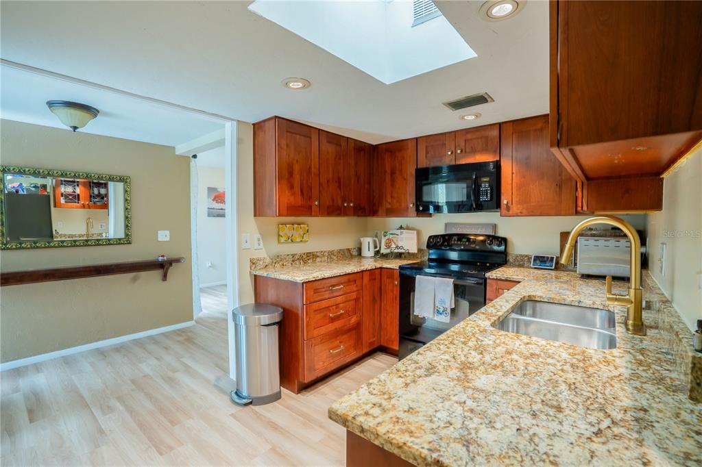 A kitchen features wood cabinets, granite countertops, a stainless steel stove, and a skylight — 3289 FAIRHAVEN LANE UNIT 112, SARASOTA, FL