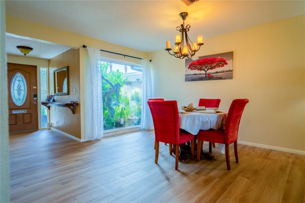 A dining room features red chairs, a round table, a chandelier, and a large window — 3289 FAIRHAVEN LANE UNIT 112, SARASOTA, FL