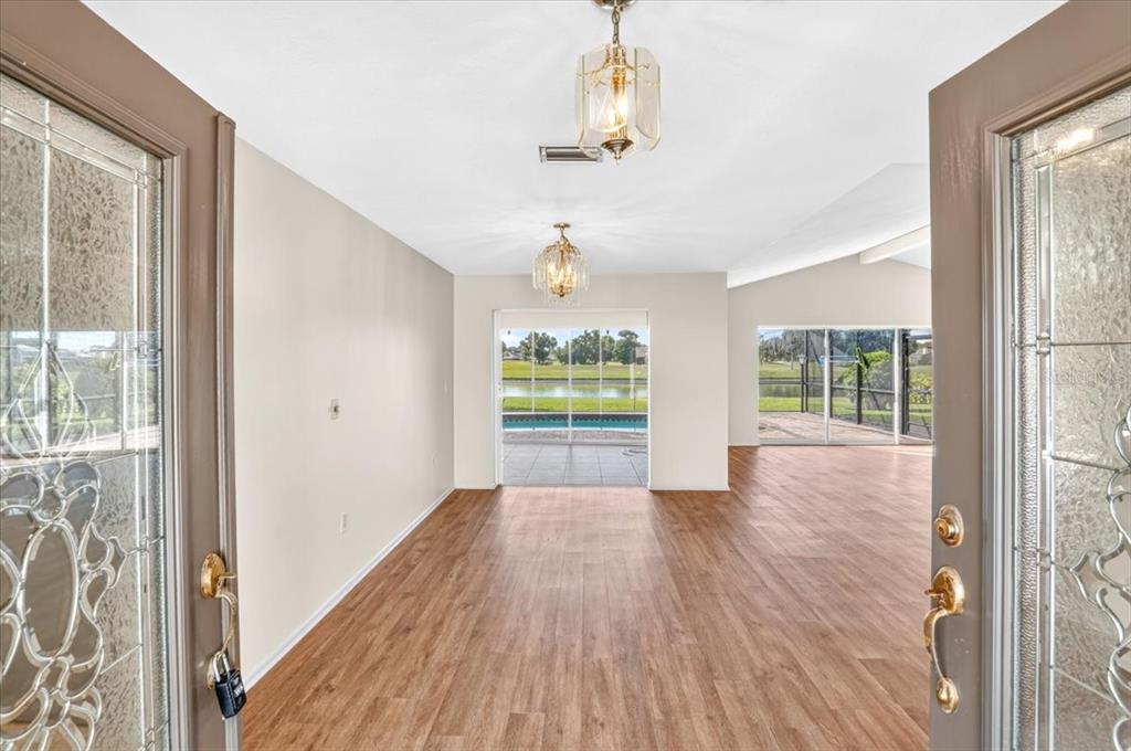 An entryway with wood-look flooring leads to a living area with views of a pool — 3504 WILDERNESS BOULEVARD W, PARRISH, FL
