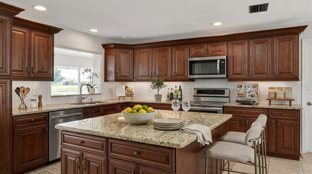 A kitchen with dark wood cabinets, granite countertops, a central island, and stainless steel appliances — 3504 WILDERNESS BOULEVARD W, PARRISH, FL