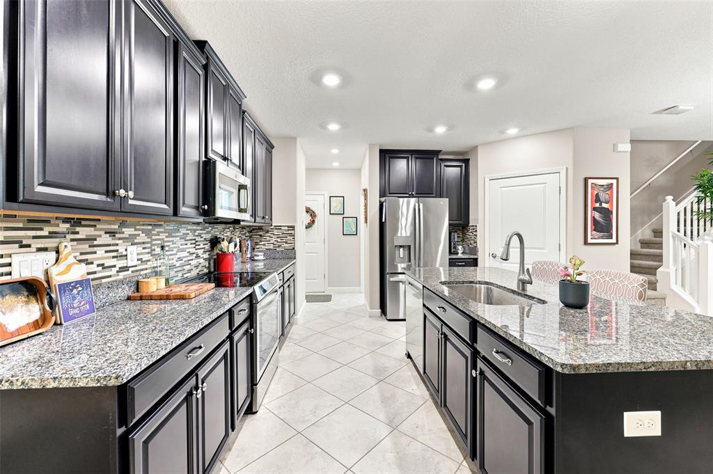 A kitchen features dark cabinets, granite countertops, a central island, and light-colored tile flooring — 5305 STOIC VALE DRIVE, WIMAUMA, FL