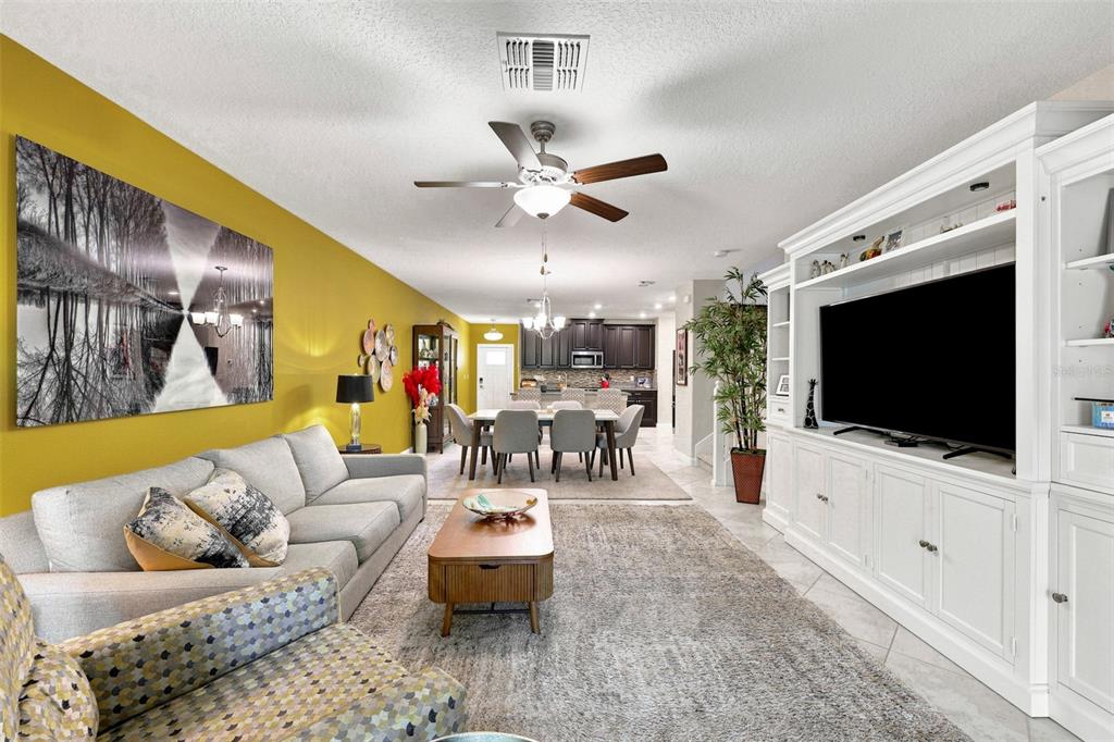 A living room with a yellow wall, grey sofa, white entertainment center, and dining area — 5305 STOIC VALE DRIVE, WIMAUMA, FL