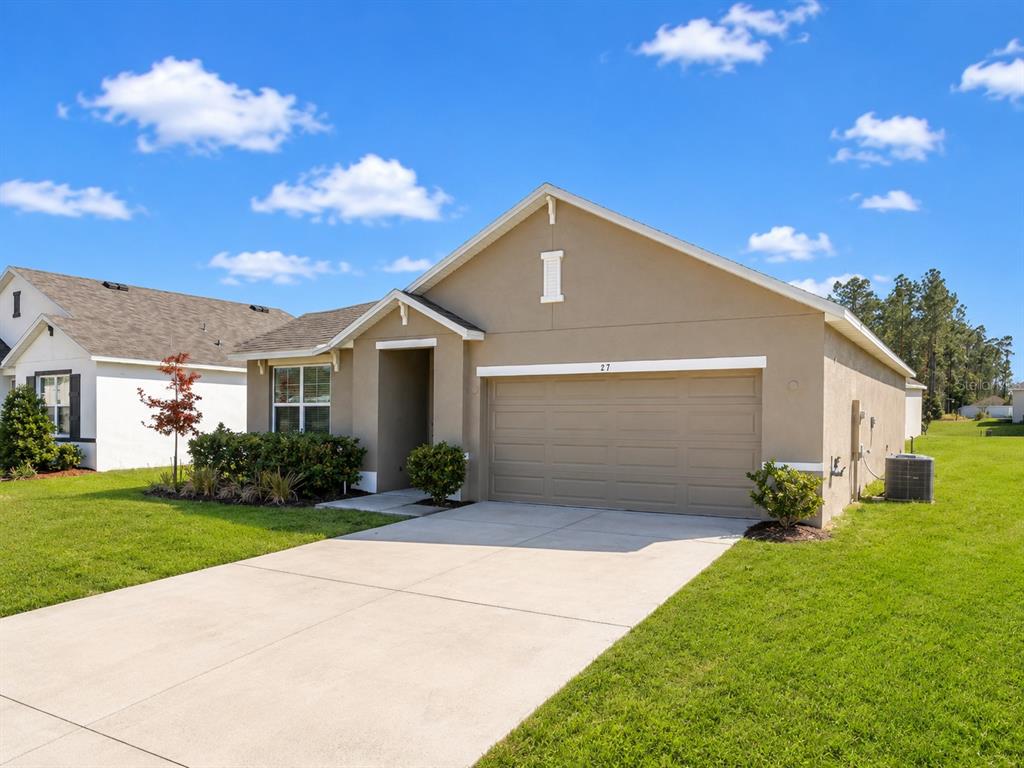 A tan, single-story suburban house with a two-car garage and a concrete driveway — 27 HICKORY COURSE LANE, OCALA, FL