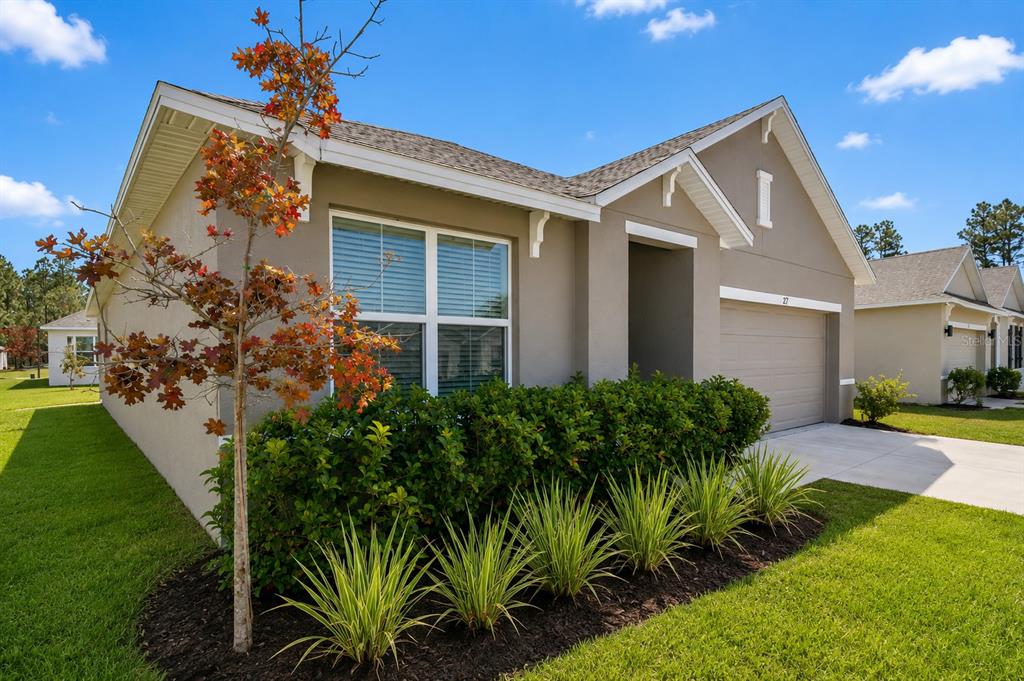 A single-story house exterior with a tan stucco facade, a garage, and front landscaping — 27 HICKORY COURSE LANE, OCALA, FL