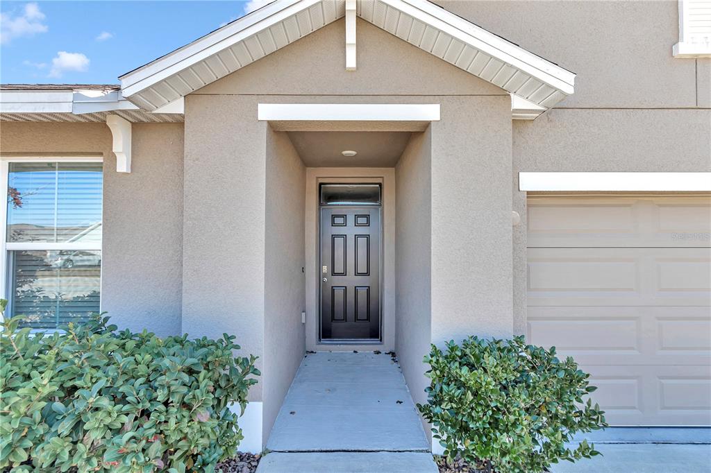 The exterior of a house features a tan stucco facade, a dark front door, and landscaping — 27 HICKORY COURSE LANE, OCALA, FL