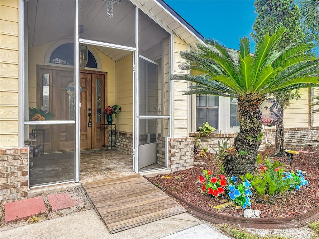 A wooden ramp leads to a screened-in front porch with a wooden door and landscaping — 1406 KINGSTON WAY, KISSIMMEE, FL