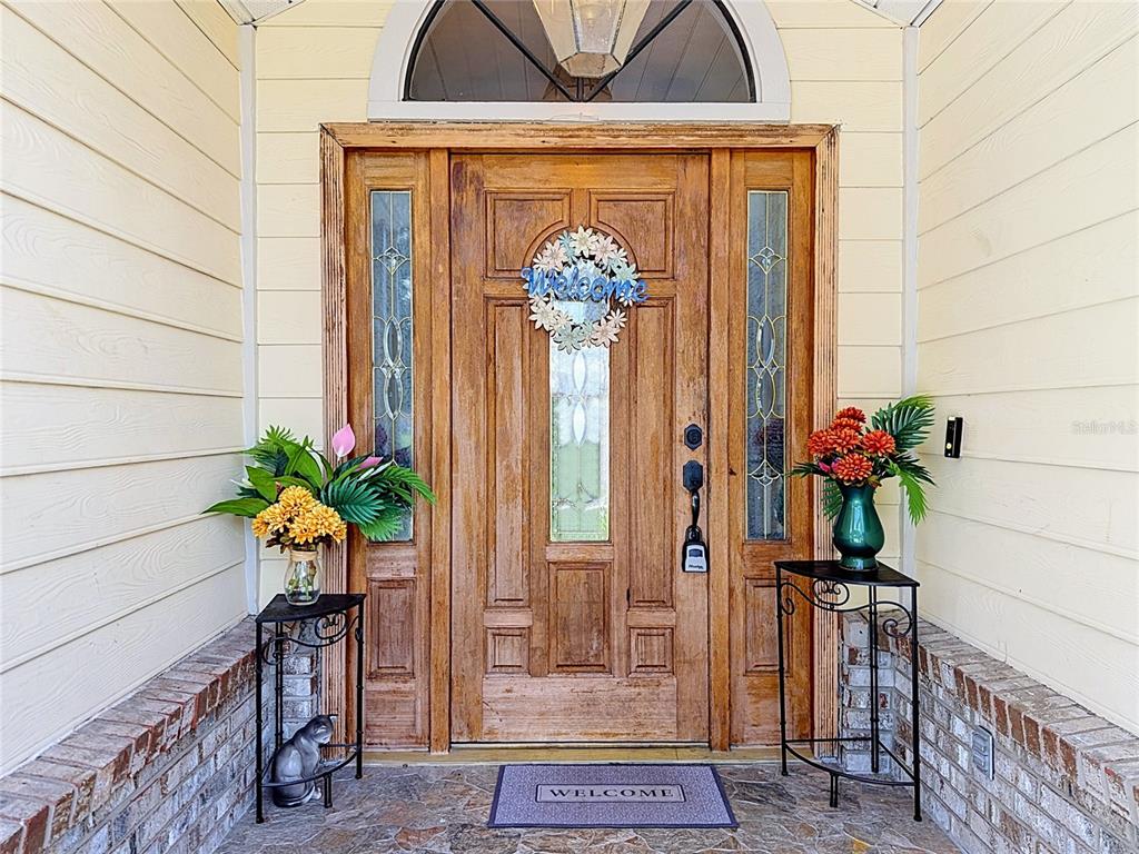 A wooden front door with sidelights and a transom window sits on a brick porch — 1406 KINGSTON WAY, KISSIMMEE, FL