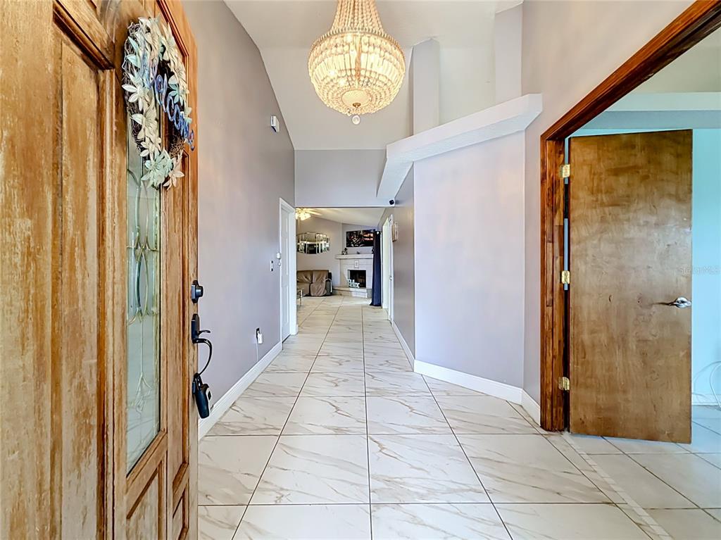 A tiled entryway features a crystal chandelier, vaulted ceilings, and a wooden front door — 1406 KINGSTON WAY, KISSIMMEE, FL
