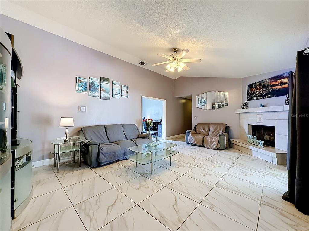 A living room features light-colored tile floors, a fireplace, and a ceiling fan — 1406 KINGSTON WAY, KISSIMMEE, FL