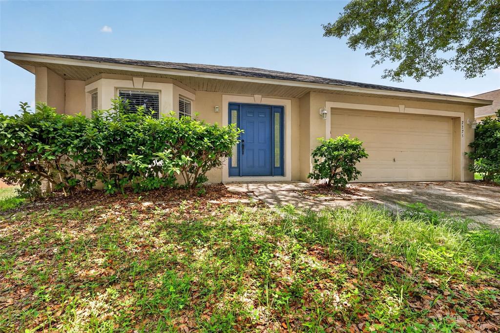 A blue front door with side windows is centered on a beige stucco house exterior — 2225 SANDRIDGE CIRCLE, EUSTIS, FL