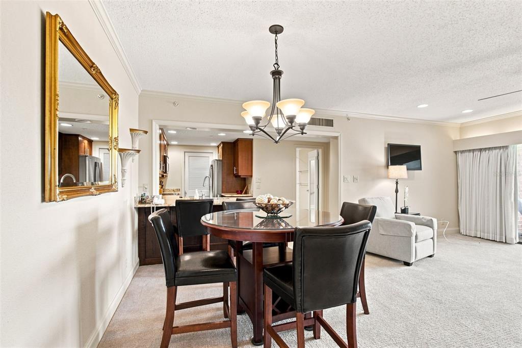 A dining area with a glass-topped table and chairs sits before an open kitchen — 36750 US HIGHWAY 19 N UNIT 04-130, PALM HARBOR, FL