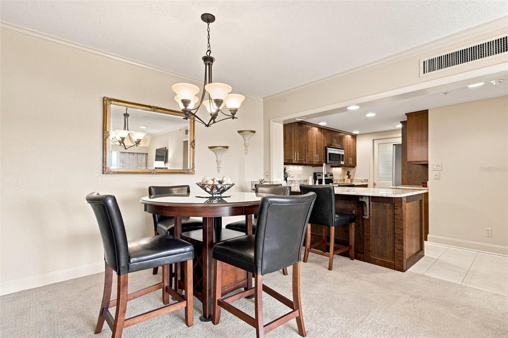 A dining area with a round table and chairs sits adjacent to an open kitchen — 36750 US HIGHWAY 19 N UNIT 04-130, PALM HARBOR, FL