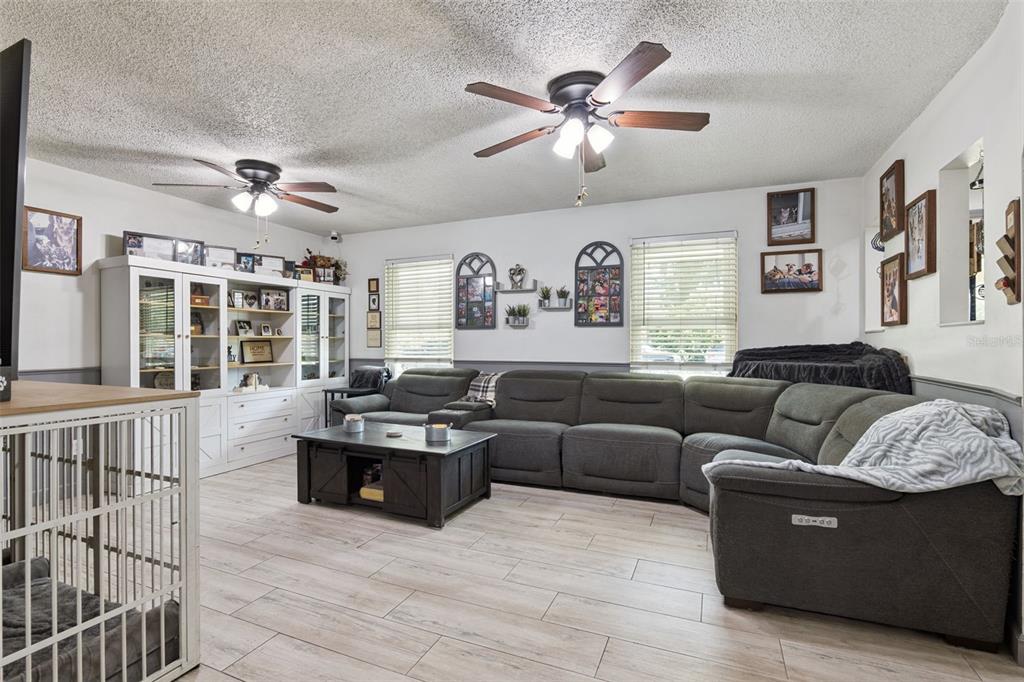 A living room features a large gray sectional sofa, a dark wooden coffee table, and ceiling fans — 1629 ORANGE TREE DRIVE, EDGEWATER, FL