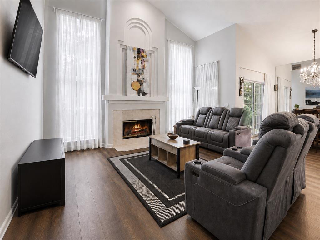 A living room features a fireplace, gray reclining furniture, a dark rug, and wood flooring — 3408 IDLEGROVE COURT, ORLANDO, FL