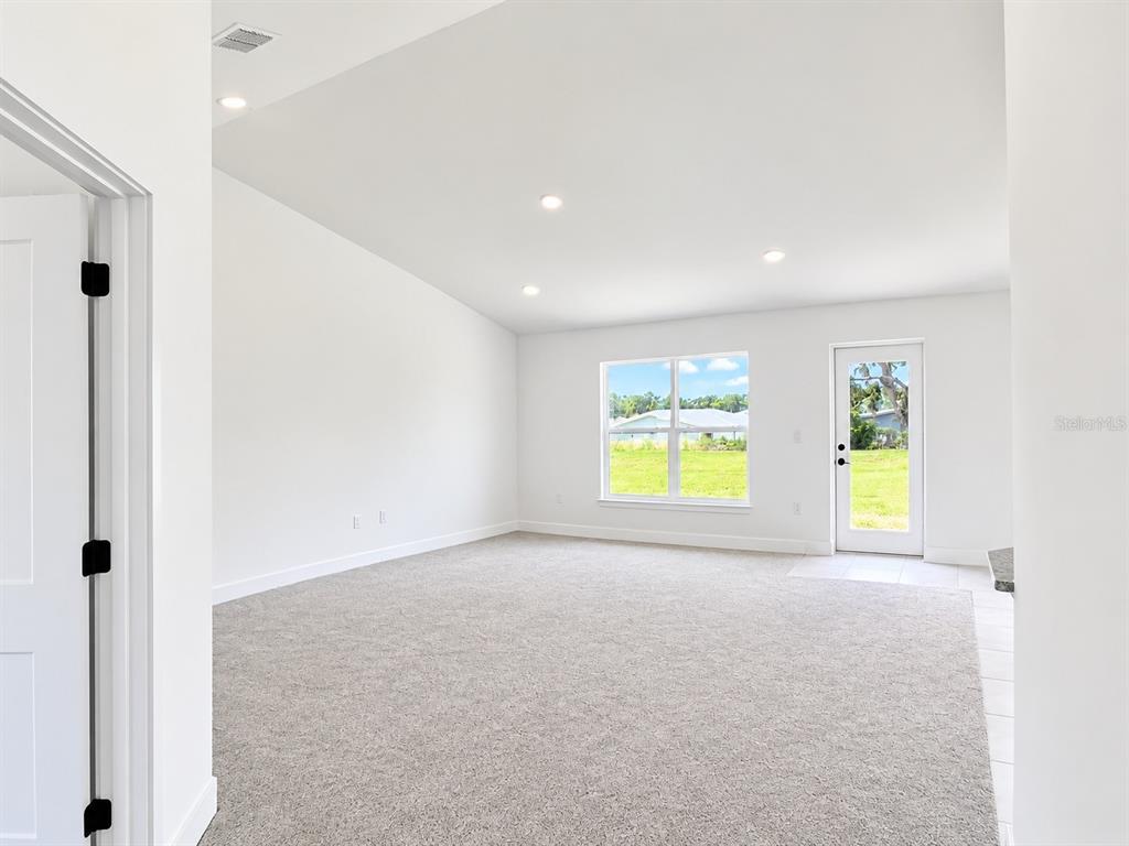 A carpeted room with a vaulted ceiling, recessed lighting, and a doorway to a bathroom — 1684 ANN ROSE WAY, LEESBURG, FL