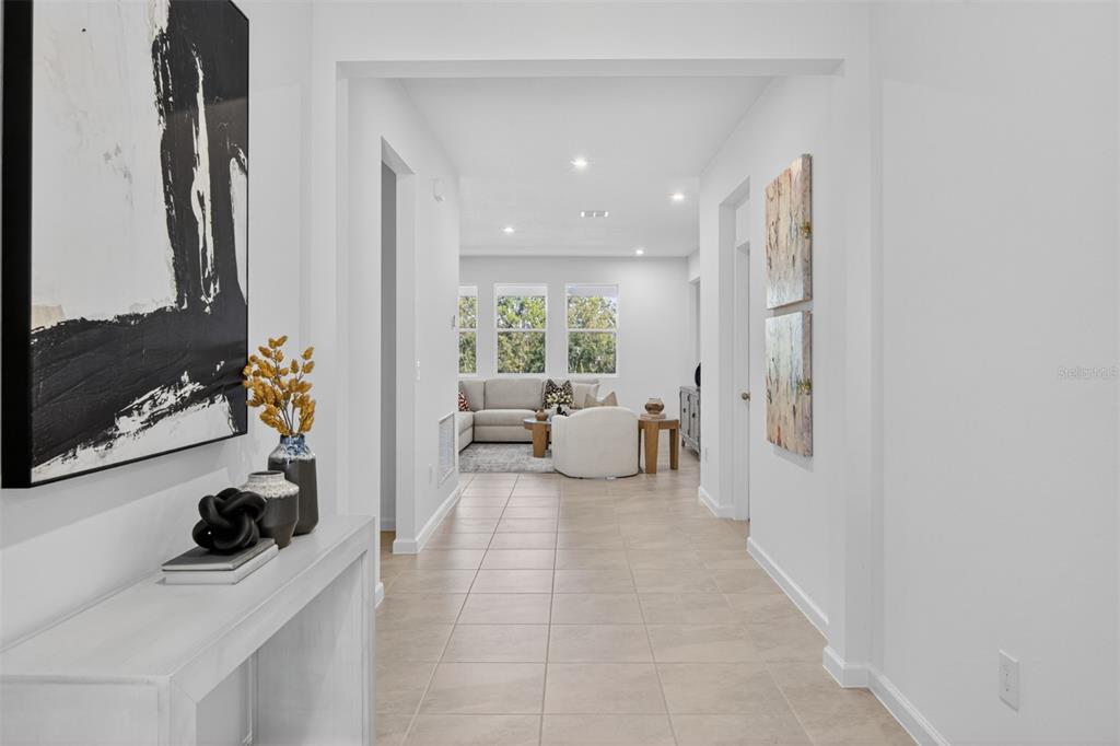 A bright hallway with tile flooring leads toward a living room with large windows — 336 FREE RANGE DRIVE, GROVELAND, FL