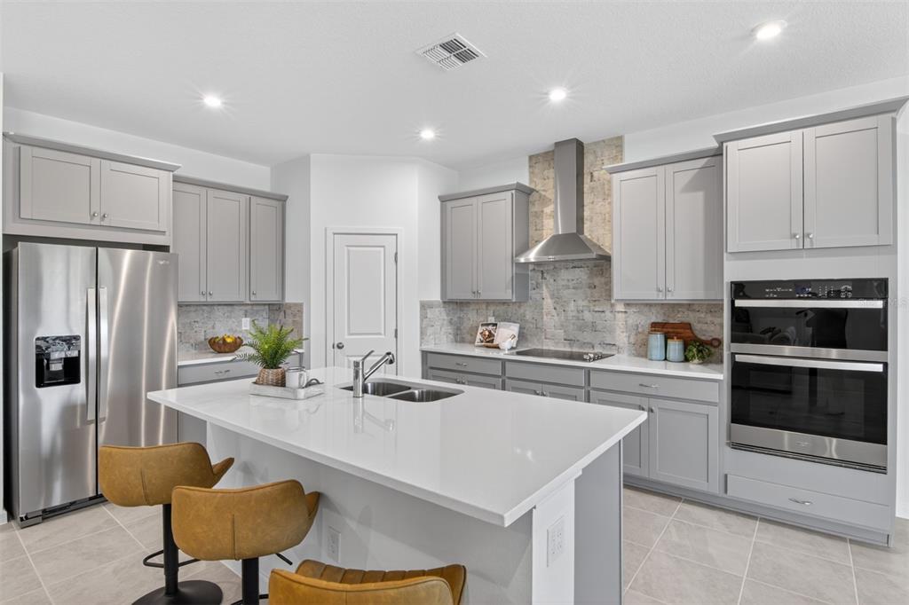 A modern kitchen features gray cabinets, a white quartz island, stainless steel appliances, and tile flooring — 336 FREE RANGE DRIVE, GROVELAND, FL