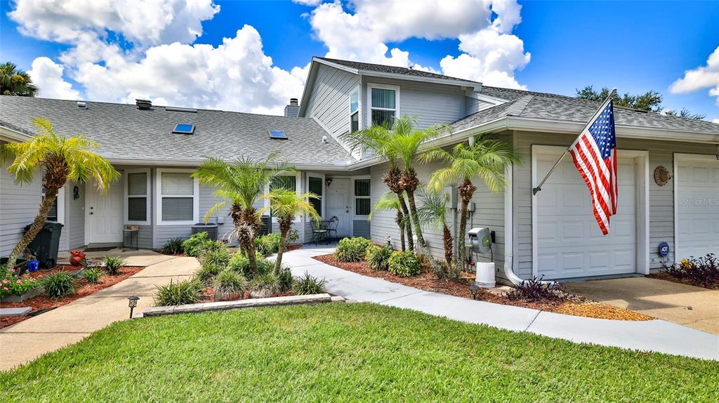 A gray-sided house with a white garage door, American flag, and palm trees in the yard — 932 MEADOW VIEW DRIVE UNIT C, PORT ORANGE, FL