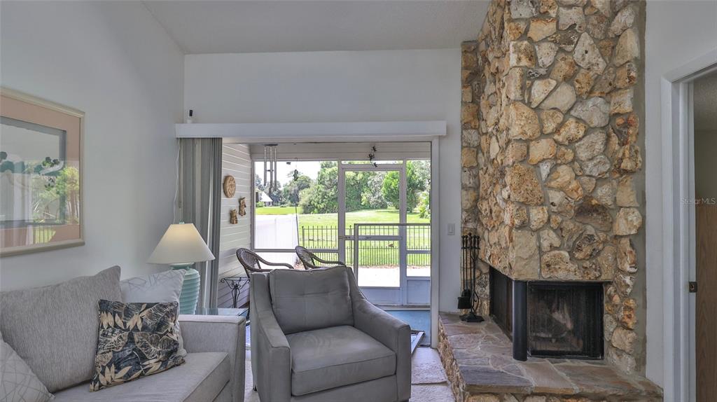 A living room features a stone fireplace, a gray armchair, and a view of a patio — 932 MEADOW VIEW DRIVE UNIT C, PORT ORANGE, FL