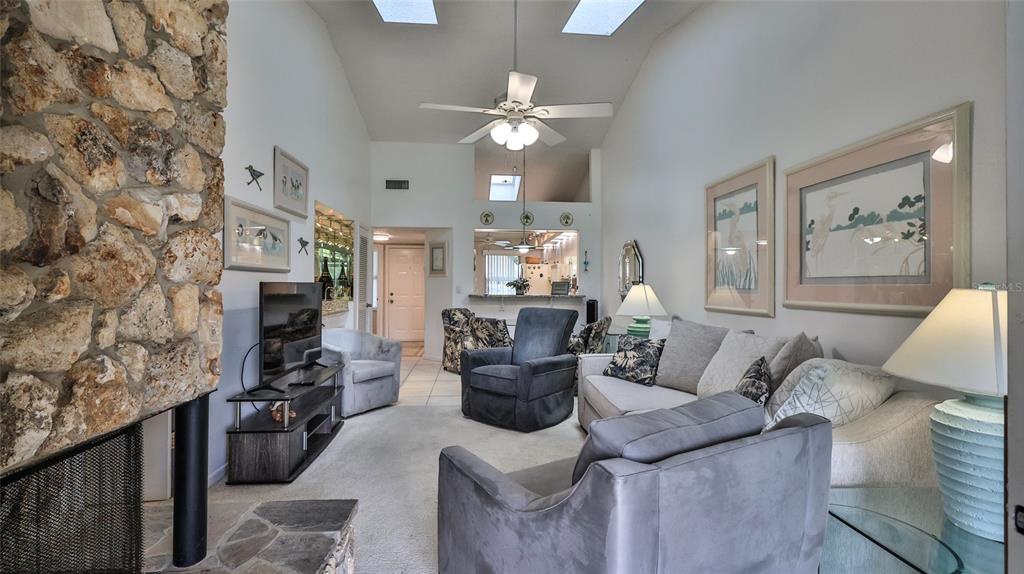 A living room features a stone fireplace, vaulted ceilings with skylights, and neutral-toned furniture — 932 MEADOW VIEW DRIVE UNIT C, PORT ORANGE, FL