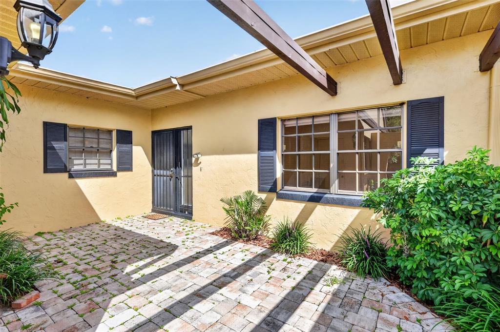 A paved patio area features a yellow stucco exterior, dark shutters, and a wooden pergola — 1111 LAKESHORE DRIVE UNIT C3, EUSTIS, FL