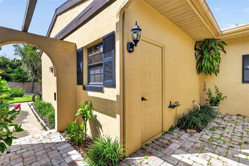 A yellow stucco exterior wall features a door, a window with shutters, and a brick patio — 1111 LAKESHORE DRIVE UNIT C3, EUSTIS, FL