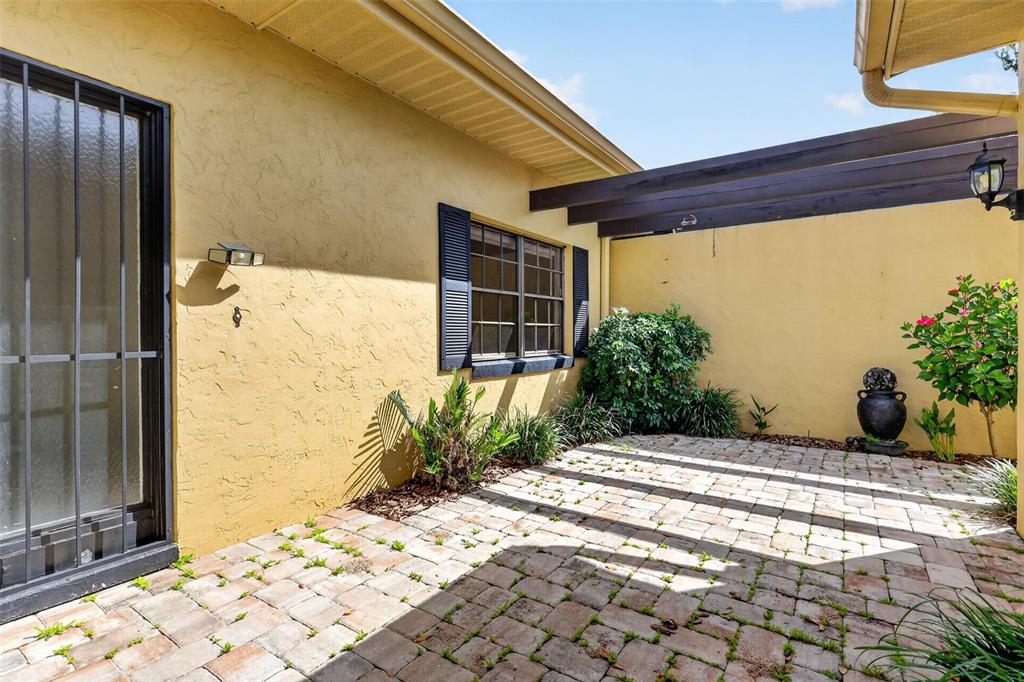 A paved patio area features a yellow stucco wall, a window with shutters, and pergola beams — 1111 LAKESHORE DRIVE UNIT C3, EUSTIS, FL