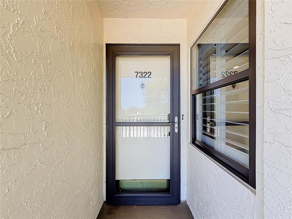 A dark-framed storm door with the number 7322 sits between textured white walls — 11945 143RD STREET UNIT 7322, LARGO, FL