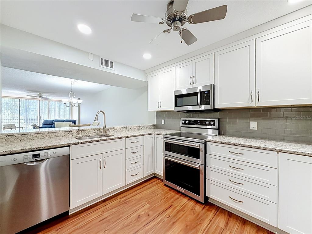 A kitchen features white cabinets, stainless steel appliances, granite countertops, and wood-look flooring — 11945 143RD STREET UNIT 7322, LARGO, FL