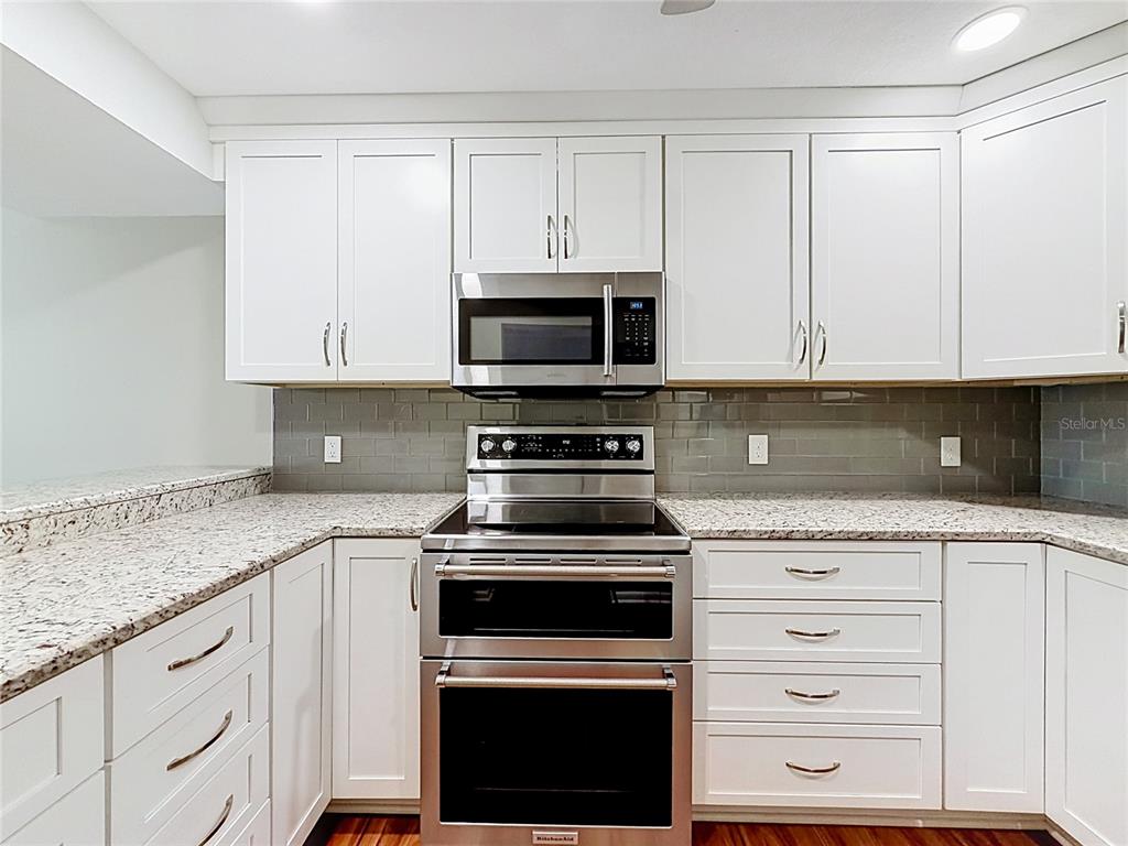 A kitchen features white cabinets, granite countertops, a stainless steel oven, and a gray backsplash — 11945 143RD STREET UNIT 7322, LARGO, FL