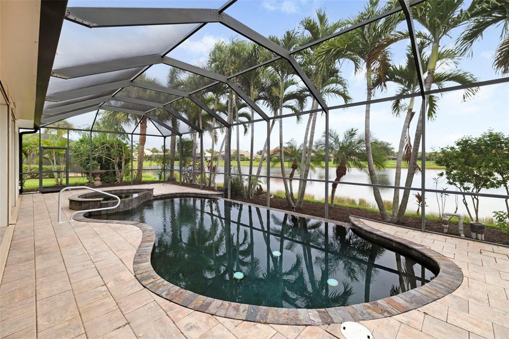 A screened-in pool and spa area with stone coping overlooking a lake and palm trees — 286 PESARO DRIVE, NOKOMIS, FL