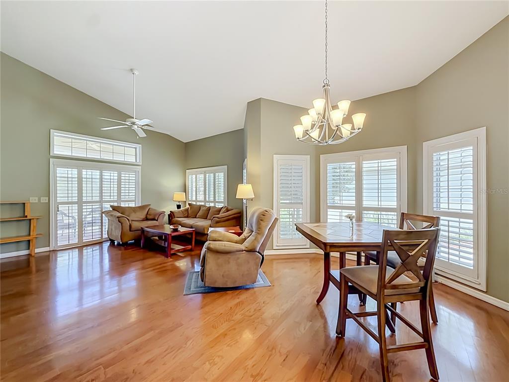 A living and dining area with hardwood floors, vaulted ceilings, and large windows with shutters — 3008 SW 41ST PLACE, OCALA, FL