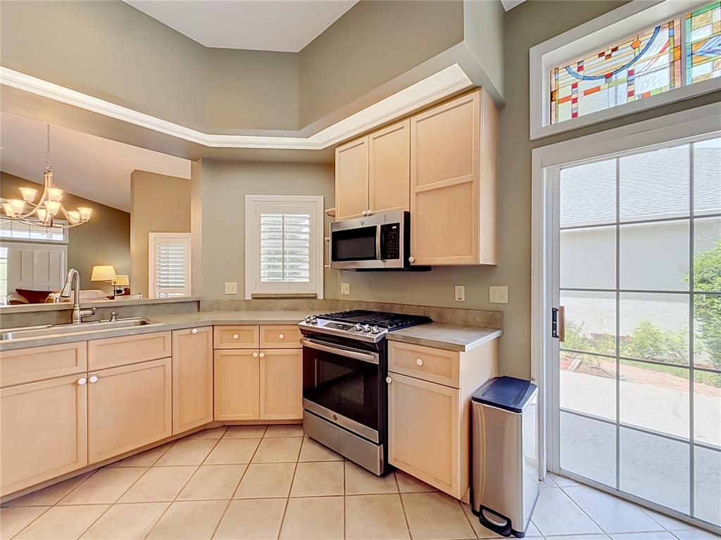 A kitchen with light wood cabinets, stainless steel appliances, tile flooring, and a glass sliding door — 3008 SW 41ST PLACE, OCALA, FL