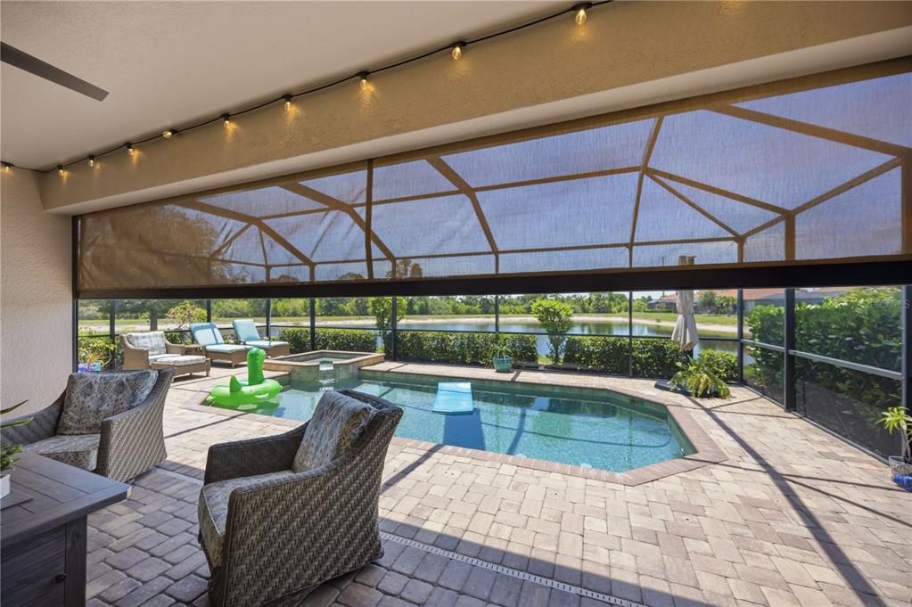 A covered patio with wicker furniture overlooks a screened-in swimming pool and a pond — 13834 VANCANZA DRIVE, VENICE, FL