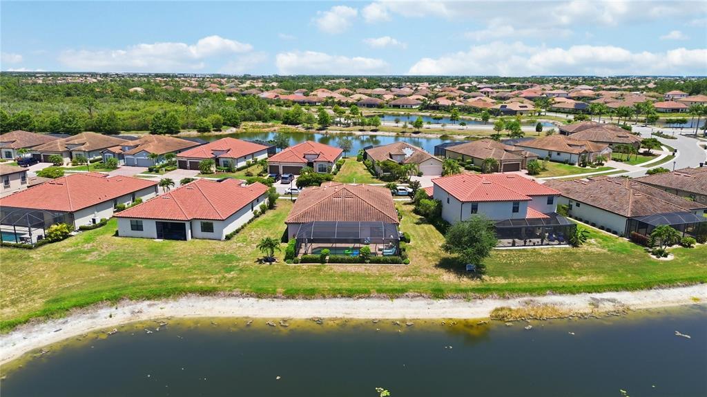 An aerial view shows several suburban houses with red tile roofs bordering a large pond — 13834 VANCANZA DRIVE, VENICE, FL